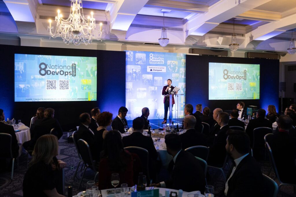 Kevin Durham on stage at the DevOps Awards 2025, with the screens and dinner tables in view