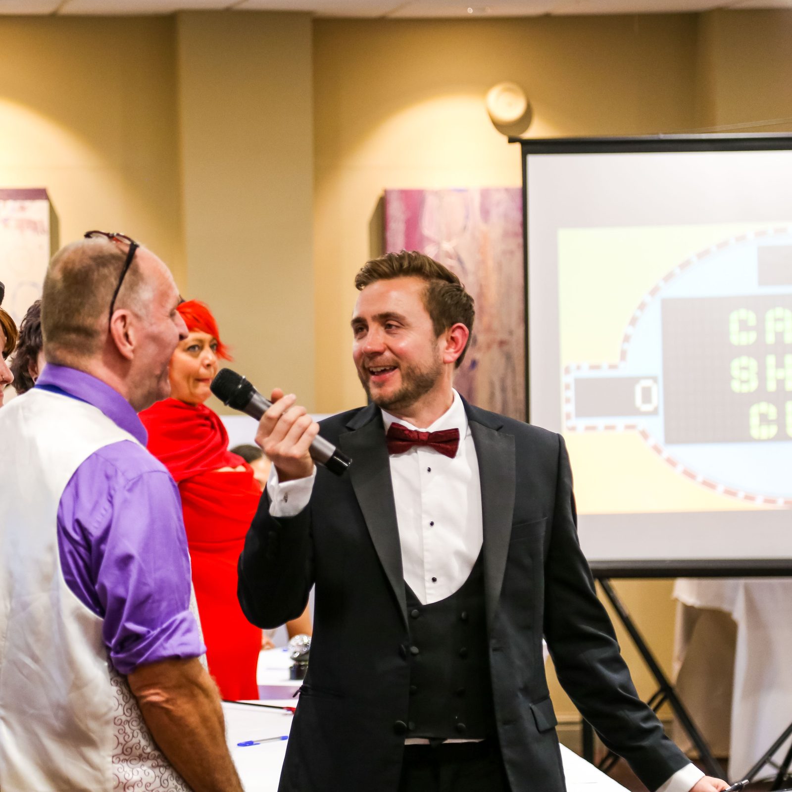 Kevin Durham hosting an interactive game show with costumed guests on stage, a Game Show Guy screen behind him