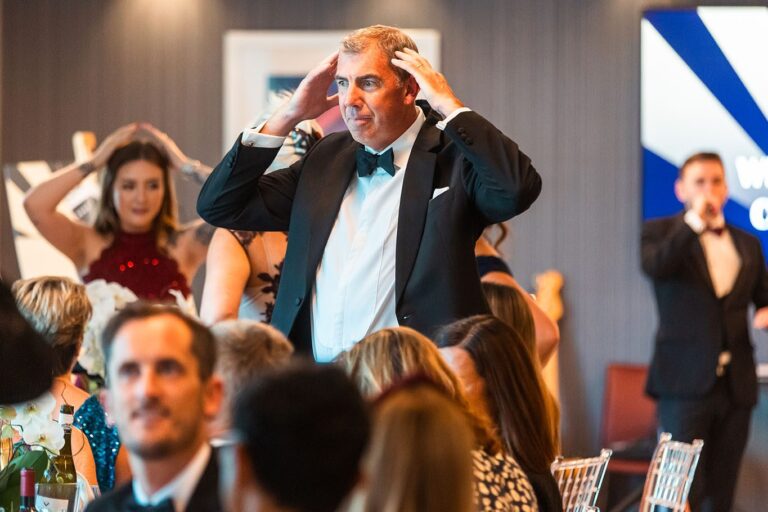 A guest with his hands on his head during Heads or Tails, Kevin Durham on the microphone behind
