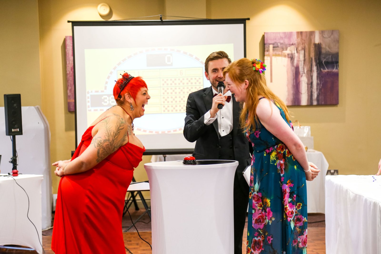 Kevin Durham hosting a live game show, with two guests at the buzzer and the board on the big screen